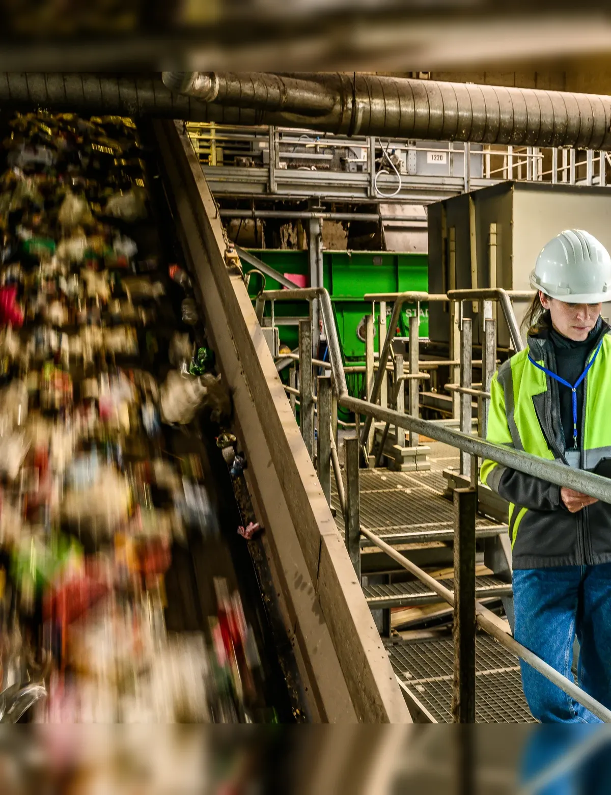 Mitarbeiterin kontrolliert den laufenden Sortierprozess einer Recyclinganlage